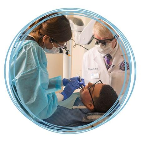 一名牙科专业的学生在为病人治疗牙齿的同时，教授在检查他们的技术