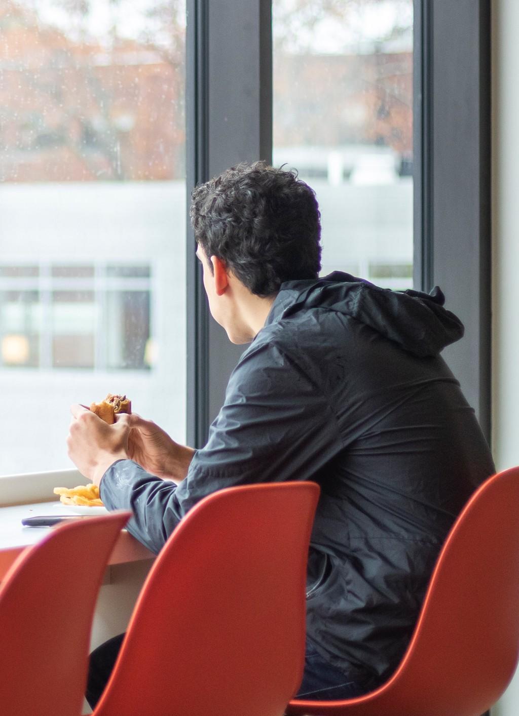 一个学生一边吃汉堡一边望着大玻璃窗